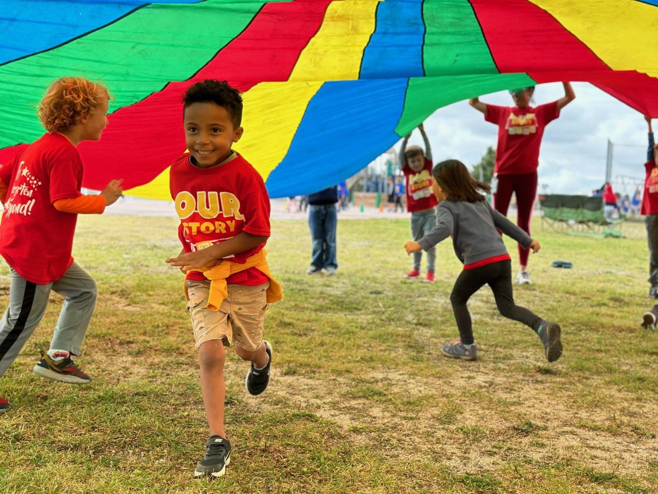 A student runs under a colorful parachute during recess.